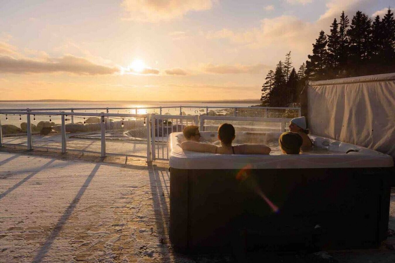 Een jacuzzi met twee personen die ontspannen, met uitzicht op een strand bij zonsondergang.