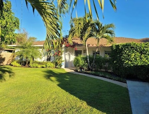 A well-maintained lawn, palm trees, and a house with a tiled roof.