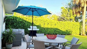 A patio with wicker furniture, a round table, and a blue umbrella. - 841 Vanderbilt Beach Bliss • Lux Waterfront Home (Naples)