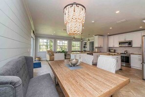 Een ruime keuken met witte kasten, een houten eettafel en een kroonluchter.