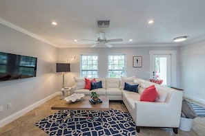 A living room with a white sofa, a coffee table, a TV, and a ceiling fan.