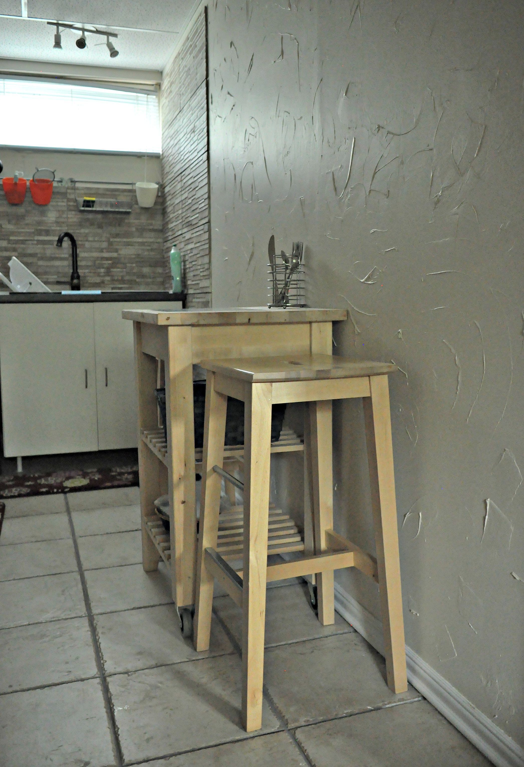 A kitchen with a sink, wooden stools, and a tiled floor.