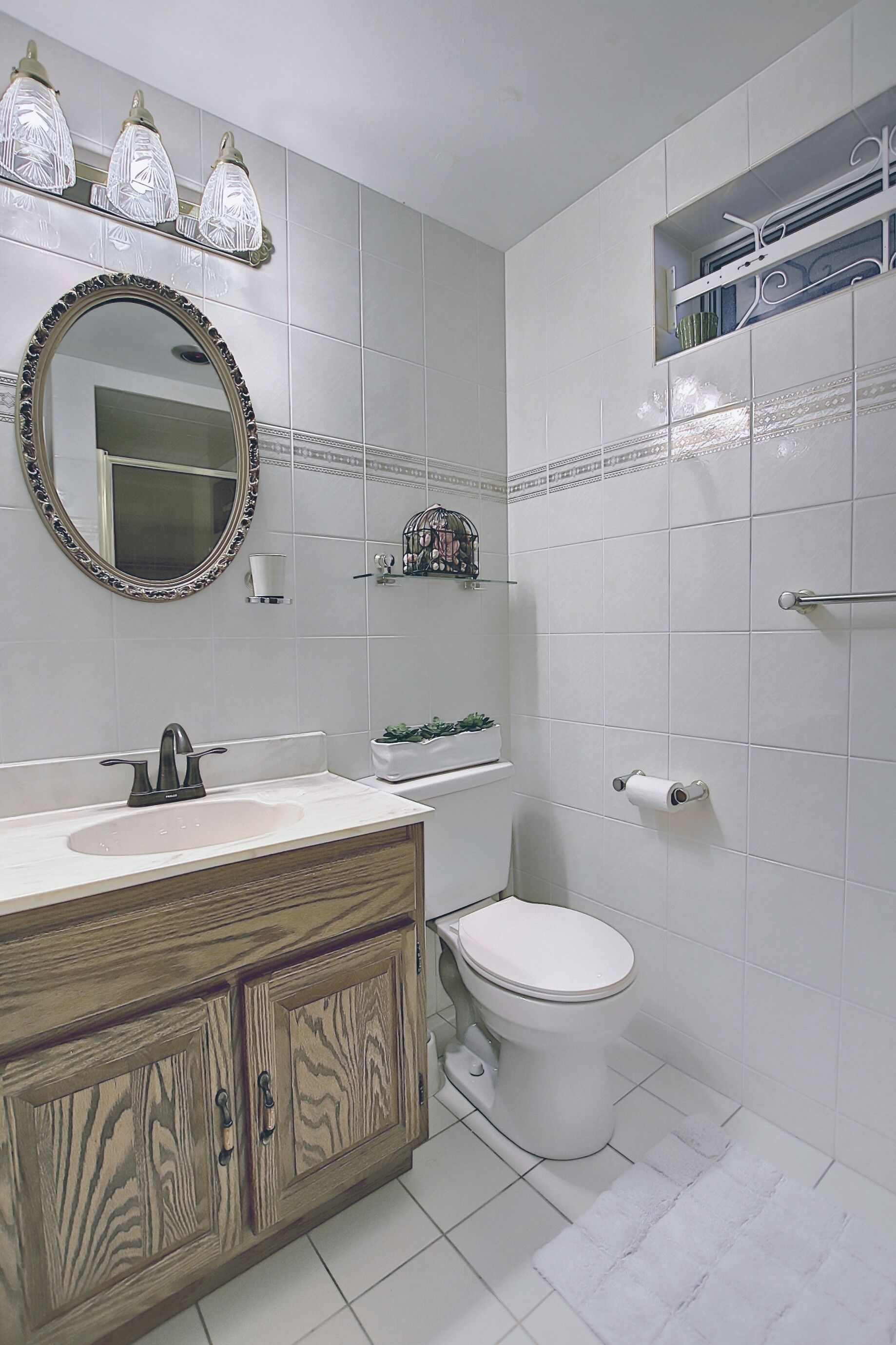 A bathroom with a wooden vanity, a white toilet, a mirror with a decorative frame, and a shelf with toiletries.