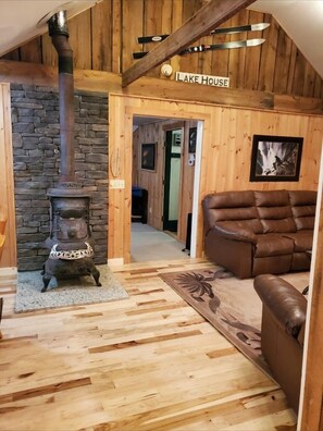Un intérieur rustique avec une cheminée en pierre, un plancher en bois, un canapé en cuir et une enseigne indiquant «
Maison au bord du lac
».