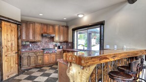 A kitchen with wooden cabinets, a granite countertop, and a bar area with stools. - Castle Glen Dream Estate! Spa, movie theater, lake and mountain views! (Big Bear)