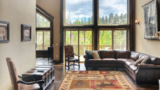 A spacious living room with a large window, a wooden ceiling, and a cozy seating area. - Castle Glen Dream Estate! Spa, movie theater, lake and mountain views! (Big Bear)