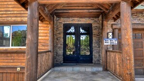 A wooden lodge entrance with a stone facade, a black double door, and a stone staircase leading up. - Castle Glen Dream Estate! Spa, movie theater, lake and mountain views! (Big Bear)