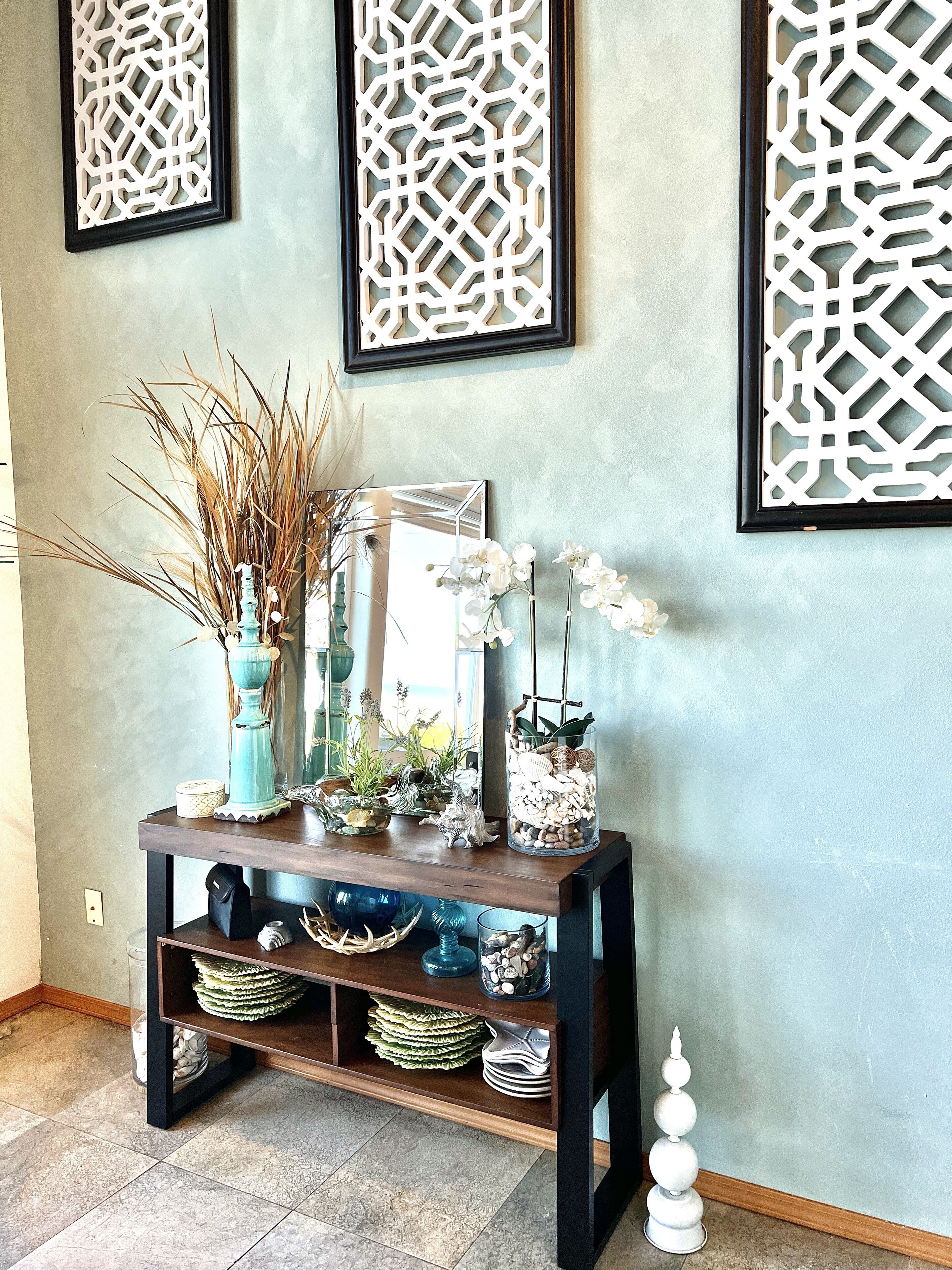 A wooden console table with decorative items, a mirror, and a wall with geometric patterned panels.