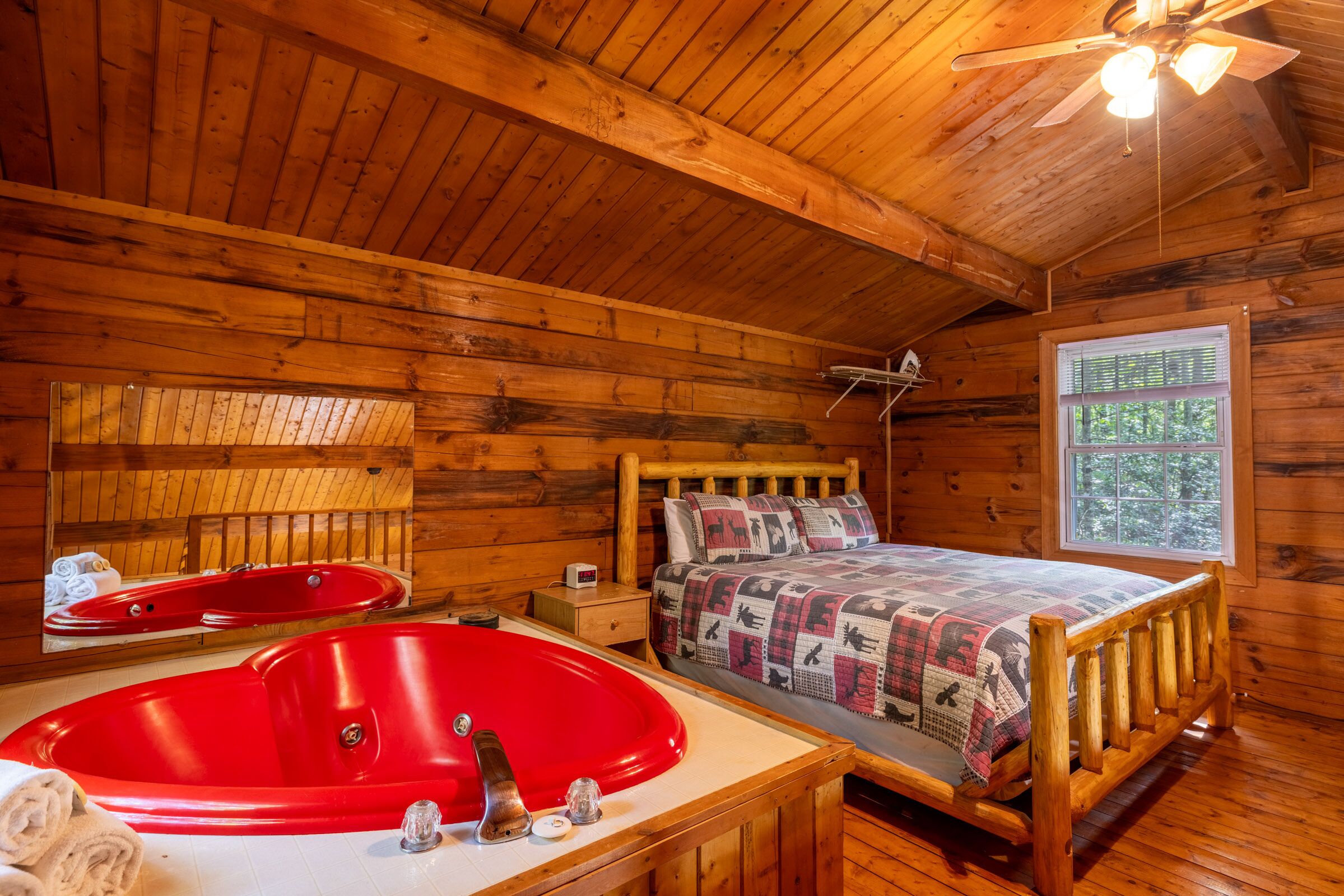Une pièce de cabane en bois comprenant un lit, une baignoire rouge, une fenêtre et un ventilateur de plafond.