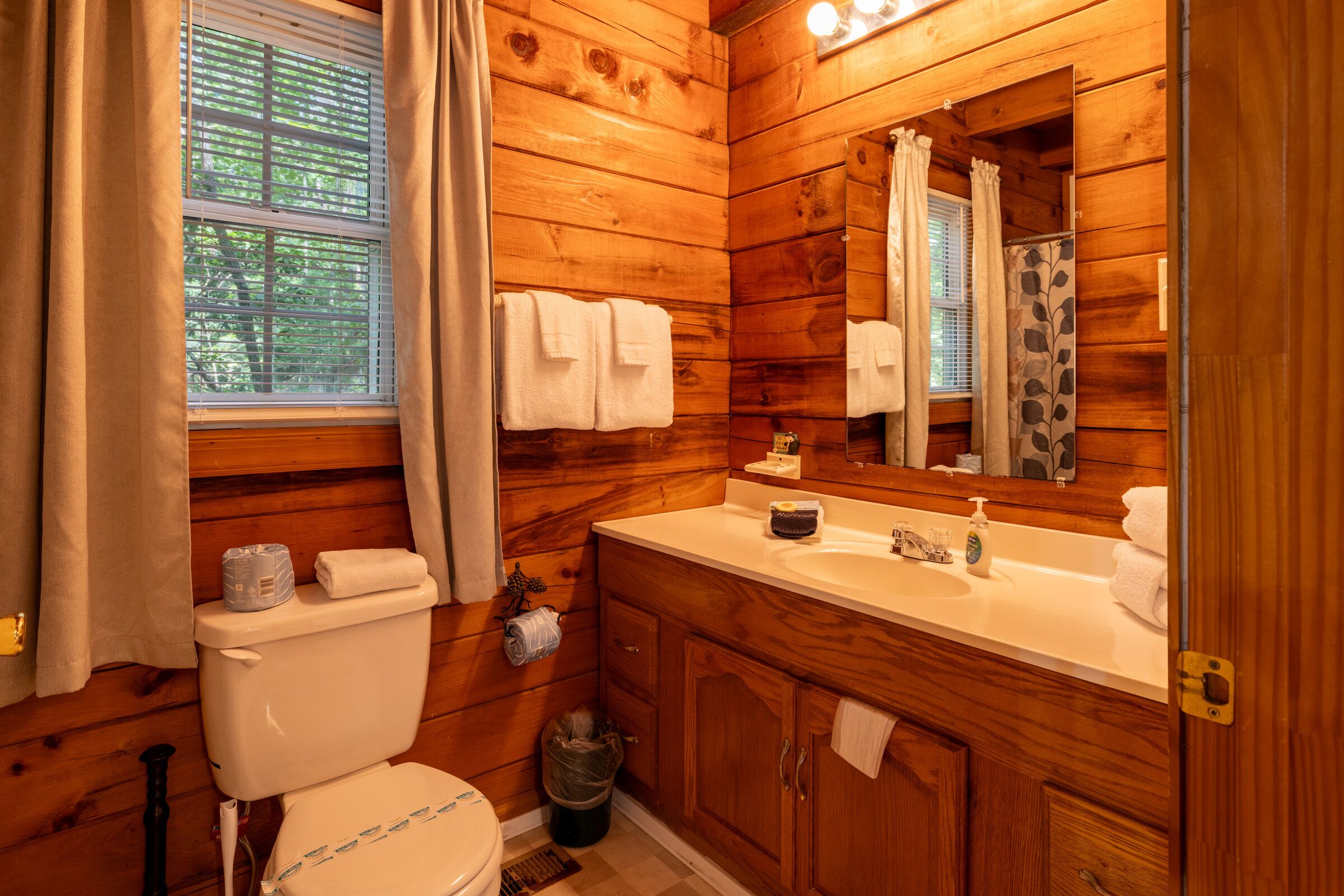 A wooden cabin bathroom with a toilet, sink, and mirror.