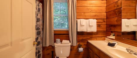 A wooden cabin bathroom with a toilet, sink, and window with curtains.