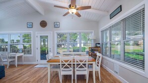 A spacious dining area with a wooden table and white chairs, large windows with blinds, and a ceiling fan.