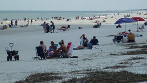 Una playa con gente relajándose en sillas y tomando el sol.
