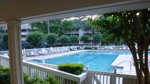 Una piscina rectangular con una cerca blanca, ubicada en un área ajardinada con árboles y arbustos.