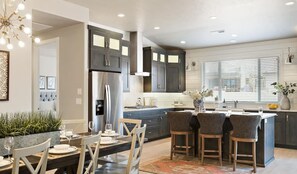 Una cocina moderna con armarios oscuros, una isla central con taburetes de bar y un comedor con mesa dispuesta para cuatro.