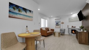 Un salon avec une table en bois, un canapé marron, une cheminée et un téléviseur fixé au mur.