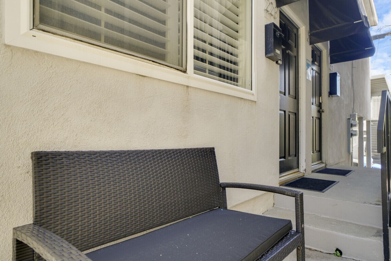A wicker chair outside a building with a white exterior, a door, and a blue awning.