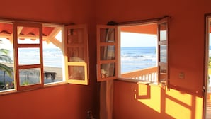 Una habitación con vista al océano a través de ventanas abiertas, una silla de madera y una cerca blanca.