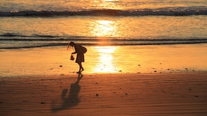 Una playa al atardecer con olas y una persona caminando sobre la arena.