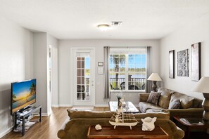 A living room with a television, a sofa, a coffee table, and a window with curtains.