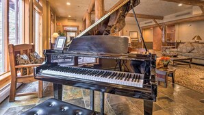 A grand piano in a spacious, well-lit lobby with a stone floor, wooden furniture, and large windows.