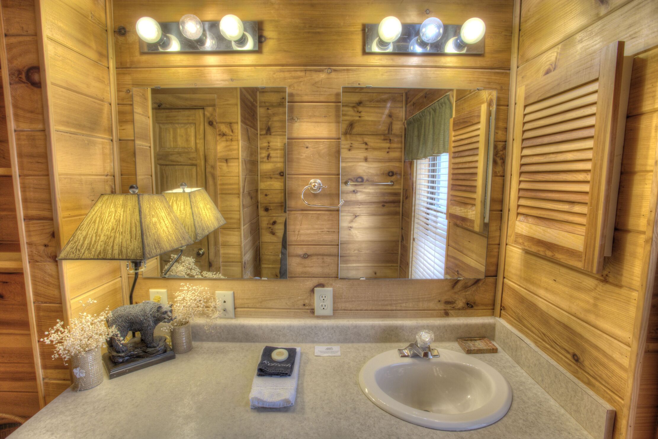 Un baño de madera con un espejo grande, un lavabo y una lámpara.