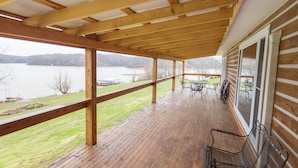 A covered wooden deck with a view of a lake, metal chairs, and a table. - Spacious Lake Barkley Retreat, 7 Queen Beds, Peaceful Cul-de-Sac , Dock Access (Cadiz)