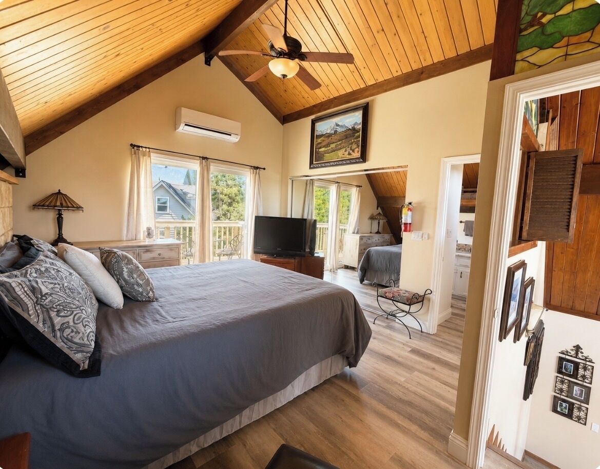 A bedroom with a bed, a ceiling fan, a television, and a view of the outdoors.