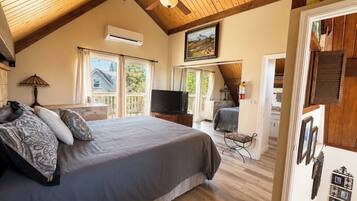 A bedroom with a bed, a ceiling fan, a television, and a view of the outdoors.