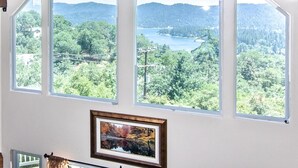 A room with large windows offering a view of a lake and forested hills. - Lake Arrowhead Luxury Escape - Amazing Views For Families, Pets & Remote Workers (Lake Arrowhead)