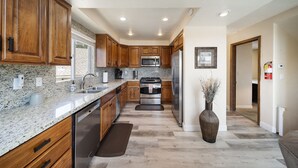 A modern kitchen with wooden cabinets, granite countertops, stainless steel appliances, and a large vase of dried flowers. - Lake Arrowhead Luxury Escape - Amazing Views For Families, Pets & Remote Workers (Lake Arrowhead)