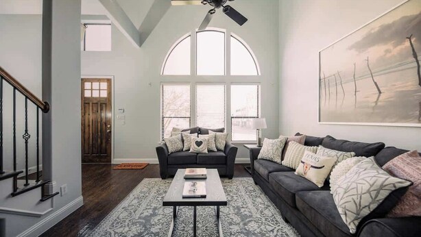 A living room with a dark sofa, a coffee table, and a large window with blinds. - Driem House Chic + Legacy Shops Walkable (Plano)