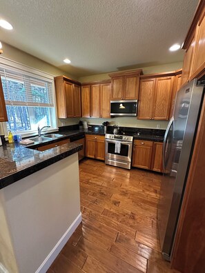 A kitchen with wooden cabinets, a stainless steel refrigerator, a microwave, and a sink.