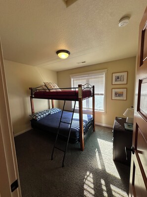 A room with a bunk bed, a desk, a lamp, and a window with blinds.