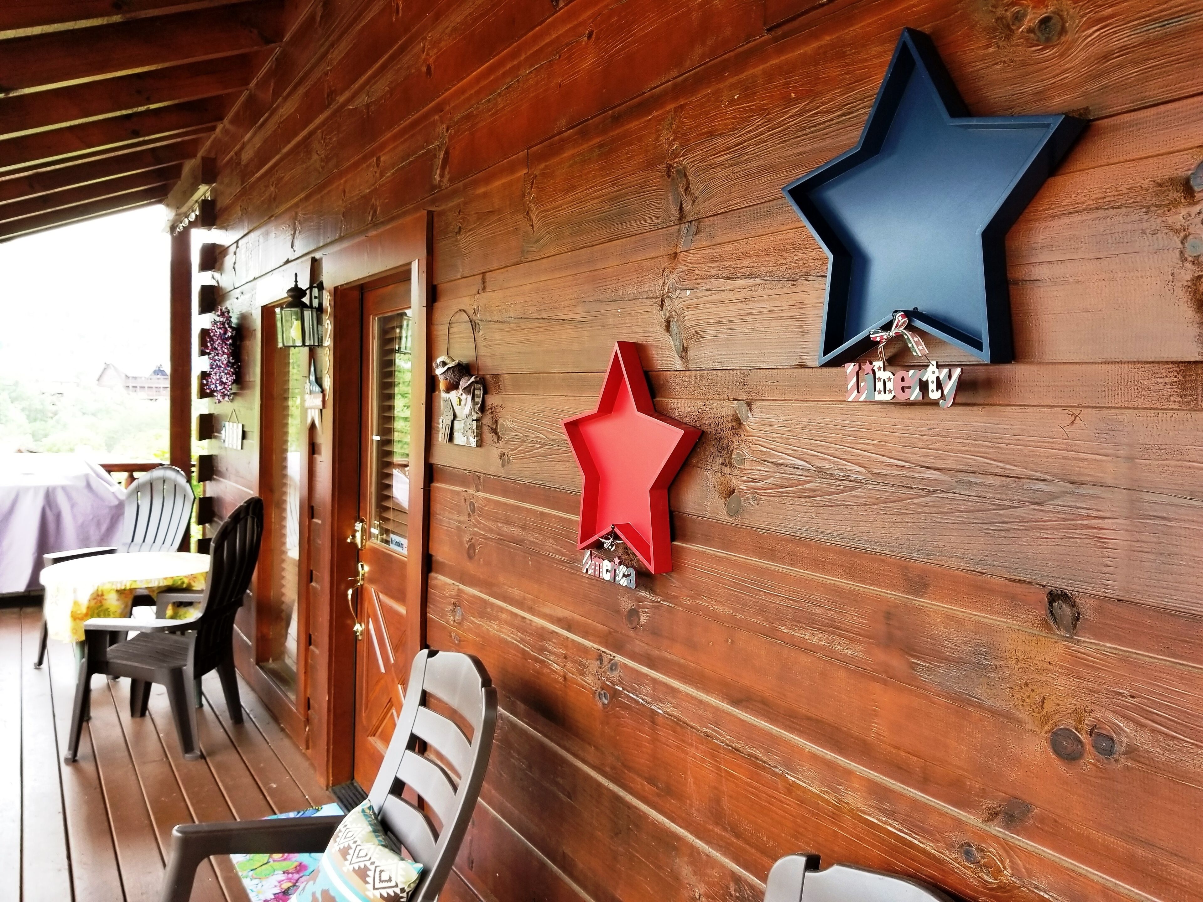 Une véranda en bois, avec une table et des chaises, décorée d’étoiles et d’une enseigne sur laquelle on peut lire « The Cabin ».