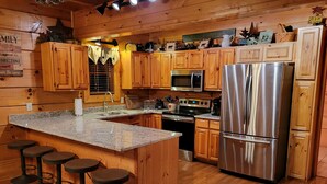 A kitchen with wooden cabinets, a stainless steel refrigerator, a microwave, and a stove. There are four stools at the island. - !BEST LOCATION! RESERVE NOW FOR SPRING BREAK AND SUMMER! BEARFOOT CORNER CABIN!  (Pigeon Forge)