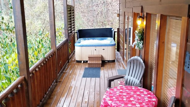 A wooden deck with a hot tub, a table with a red floral tablecloth, and two chairs. - !BEST LOCATION! RESERVE NOW FOR SPRING BREAK AND SUMMER! BEARFOOT CORNER CABIN!  (Pigeon Forge)