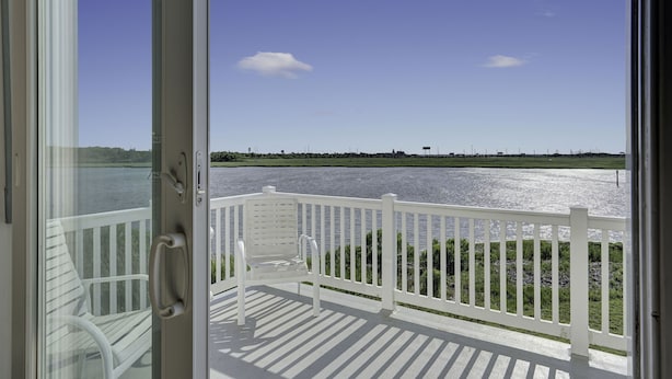 A view from a balcony with a white railing, overlooking a body of water and a distant shoreline. - Waterfront Mansion 6BR Sleeps 18 Game RM
Hot Tub & SUNSET VIEWS elevator Access (Atlantic City)