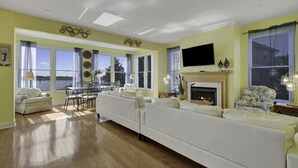 A spacious living room with a large white sofa, a fireplace, and a television mounted on the wall. - Waterfront Mansion 6BR Sleeps 18 Game RM
Hot Tub & SUNSET VIEWS elevator Access (Atlantic City)