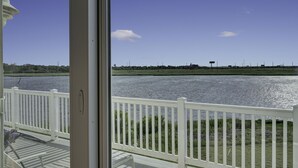 A view from a room with a white railing overlooking a body of water, a grassy area, and distant buildings. - Waterfront Mansion 6BR Sleeps 18 Game RM
Hot Tub & SUNSET VIEWS elevator Access (Atlantic City)