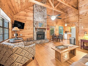 A cozy cabin interior with a stone fireplace, wooden furniture, and a television mounted on the wall. - Country Charm D - Cozy Pet Friendly Cabin in Helen (Helen)