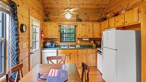 A wooden cabin kitchen with a dining table, chairs, a refrigerator, a microwave, and a ceiling fan. - Country Charm D - Cozy Pet Friendly Cabin in Helen (Helen)