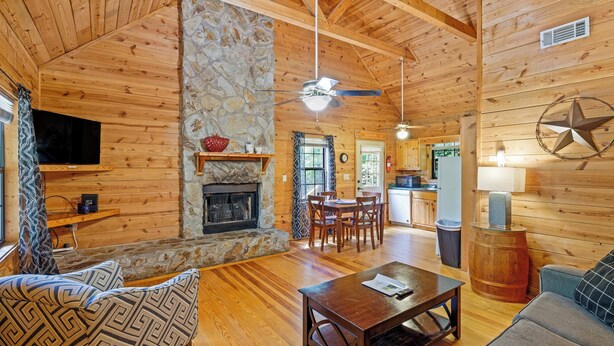 A cozy cabin interior with a stone fireplace, wooden walls, a dining area, and a kitchen. - Country Charm D - Cozy Pet Friendly Cabin in Helen (Helen)