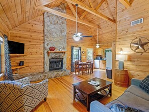 A cozy cabin interior with a stone fireplace, wooden walls, a dining area, and a kitchen. - Country Charm D - Cozy Pet Friendly Cabin in Helen (Helen)