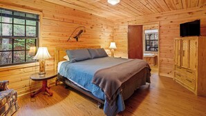 A wooden cabin bedroom with a bed, two bedside lamps, a ceiling fan, and a window with blinds. - Country Charm D - Cozy Pet Friendly Cabin in Helen (Helen)