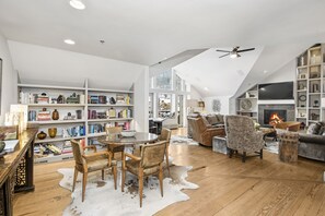 A spacious living room with a high ceiling, a fireplace, a large bookshelf, and a dining area with a round table and chairs. - CRBC-LUX PH-LOCATION! Ski in/out, Walk to Ski School, Ice Rink, Shops, Dining! (Beaver Creek)