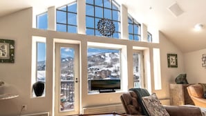 A high-ceiling living room with large windows, a fireplace, and a television. - Charlie's Slopeside: Ski-In/Out Penthouse, Sleeps 12, 3,040 Sq Ft, AC, BC Village, Walk Everywhere (Beaver Creek)