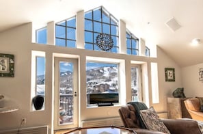 A high-ceiling living room with large windows, a fireplace, and a television. - Charlie's Slopeside: Ski-In/Out Penthouse, Sleeps 12, 3,040 Sq Ft, AC, BC Village, Walk Everywhere (Beaver Creek)