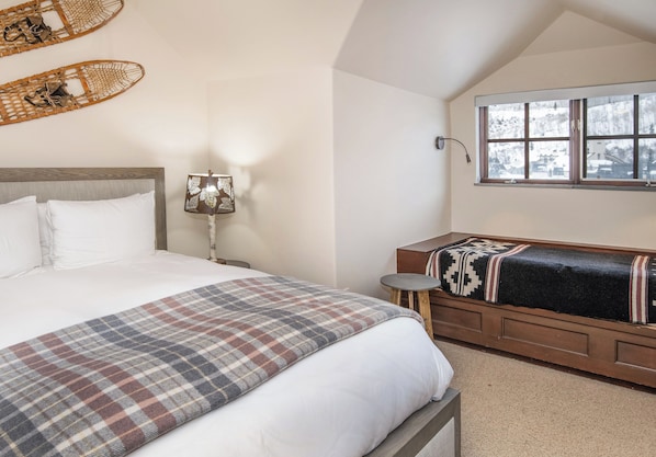 A bedroom with a bed, a bedside table with a lamp, a window with a view, and a bench with a blanket. - Charlie's Slopeside: Ski-In/Out Penthouse, Sleeps 12, 3,040 Sq Ft, AC, BC Village, Walk Everywhere (Beaver Creek)