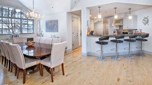 A spacious dining area with a large wooden table and multiple chairs, a kitchen with modern appliances, and a bar area with stools. - Charlie's Slopeside: Ski-In/Out Penthouse, Sleeps 12, 3,040 Sq Ft, AC, BC Village, Walk Everywhere (Beaver Creek)